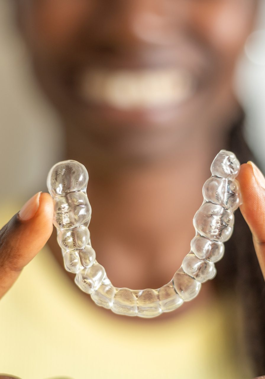 Young woman holding with two fingers an invisible dental aligner while smiling